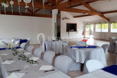 Salle lumineuse avec tables décorées de nappes blanches et chemins de table verts, prête pour un événement.