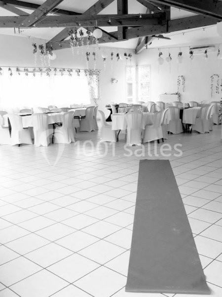 Salle de réception lumineuse avec tables rondes dressées et chaises blanches, décorée de guirlandes suspendues.