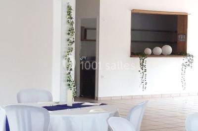Salle lumineuse avec tables décorées de nappes blanches et chemins de table verts, prête pour un événement.