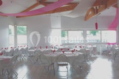 Salle lumineuse avec tables décorées de nappes blanches et chemins de table verts, prête pour un événement.