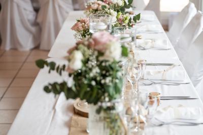 Salle lumineuse avec tables décorées de nappes blanches et chemins de table verts, prête pour un événement.