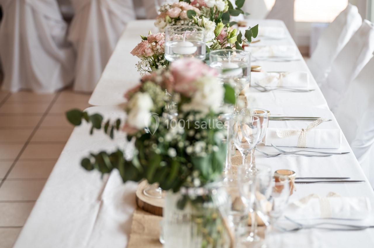 Table de réception décorée avec des fleurs, nappes blanches, vaisselle élégante et petits pains disposés.