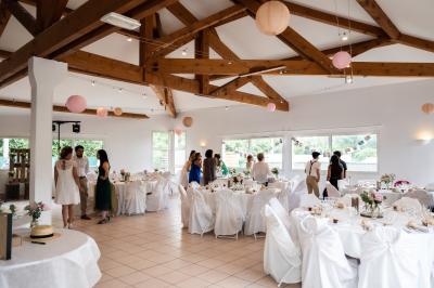 Salle lumineuse avec tables décorées de nappes blanches et chemins de table verts, prête pour un événement.