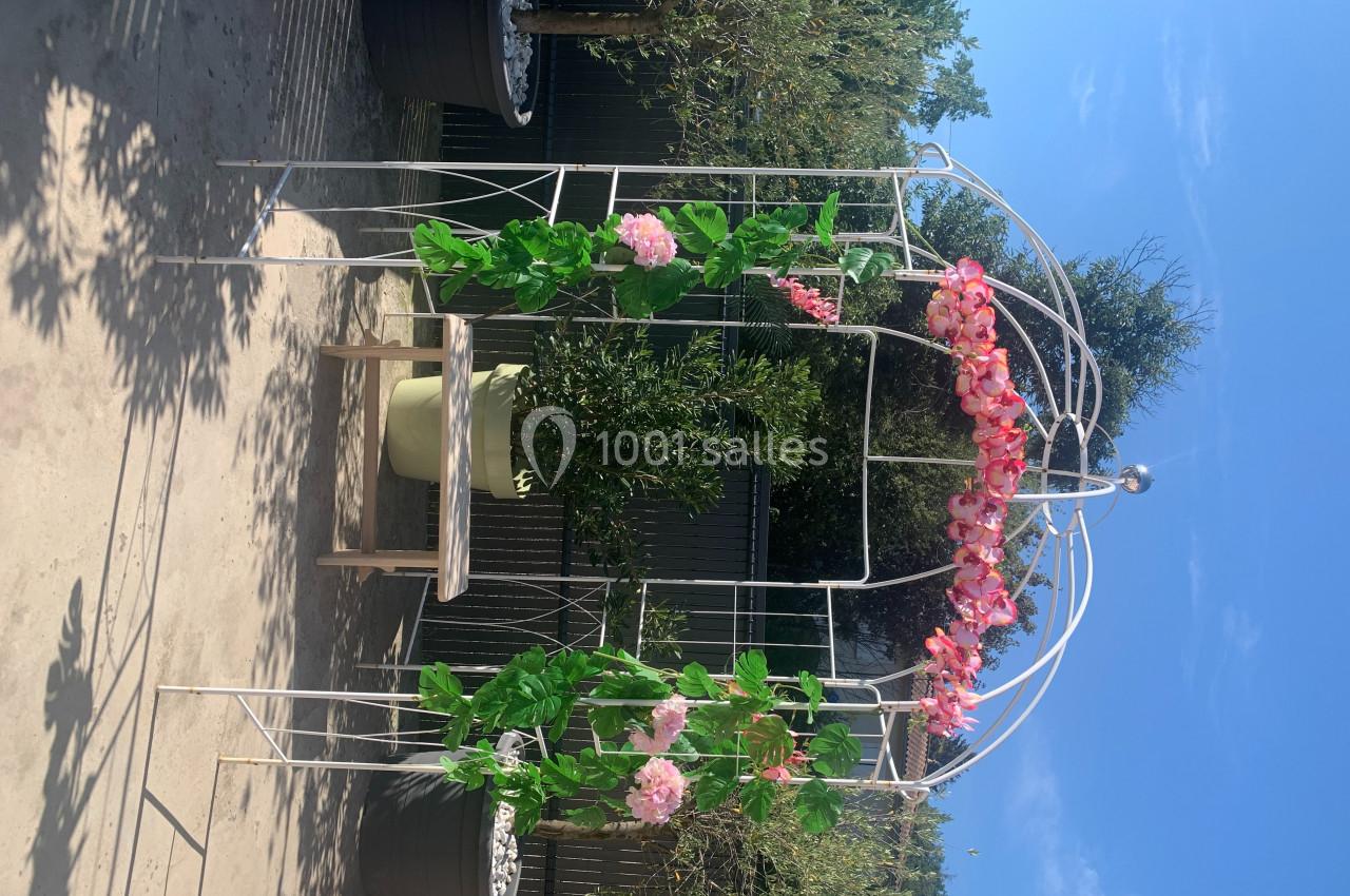 Structure métallique décorative ornée de fleurs roses et feuillages, placée dans un jardin ensoleillé.