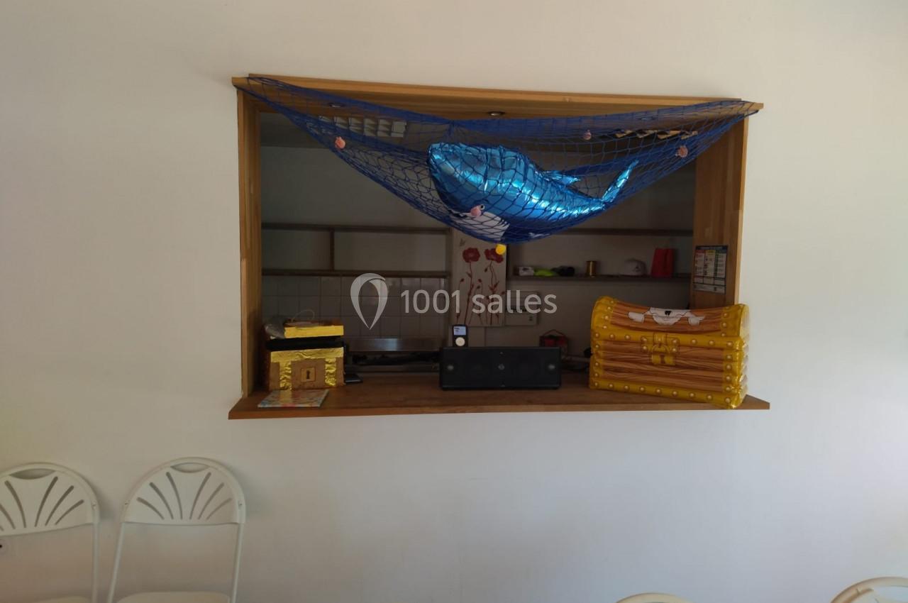 Un comptoir décoré avec un filet contenant un ballon en forme de baleine, des coffres et des chaises blanches devant.