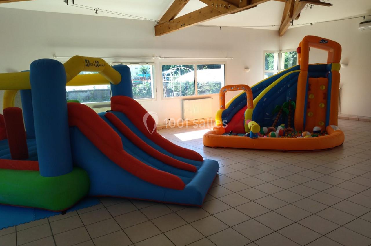 Deux structures gonflables colorées avec toboggans installées dans une salle lumineuse au sol carrelé.