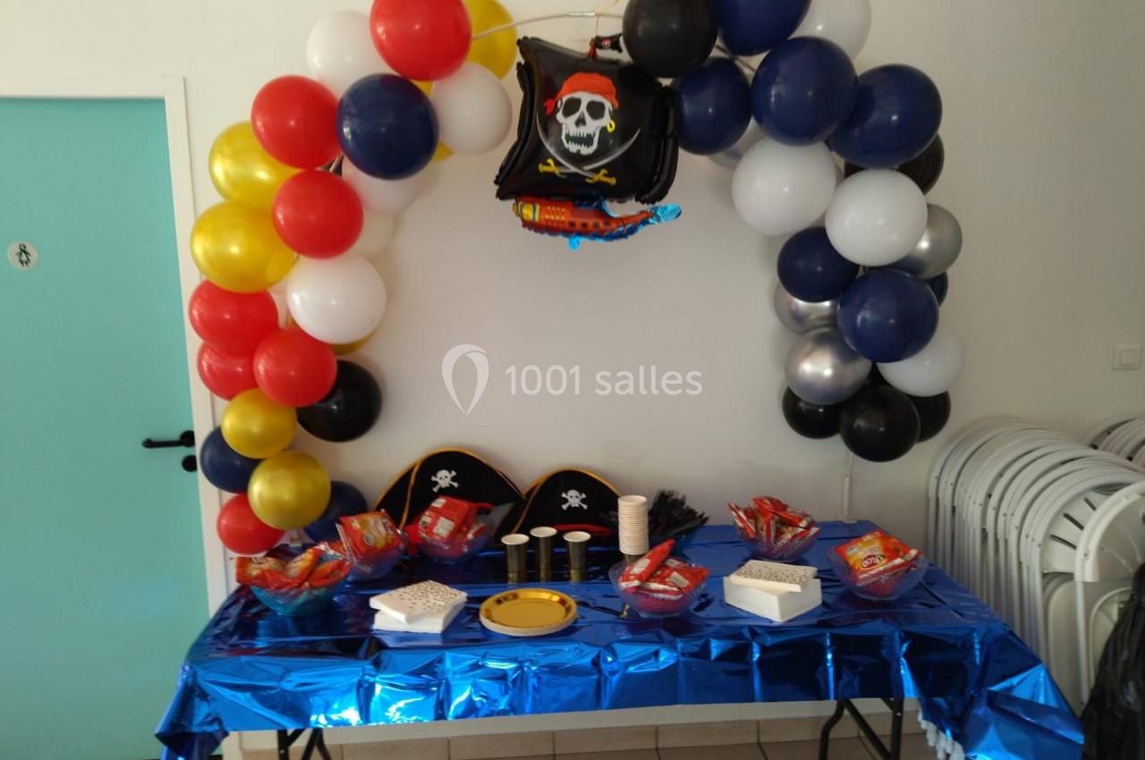 Décoration de fête sur le thème des pirates avec ballons colorés, chapeaux, snacks et nappe bleue sur une table.
