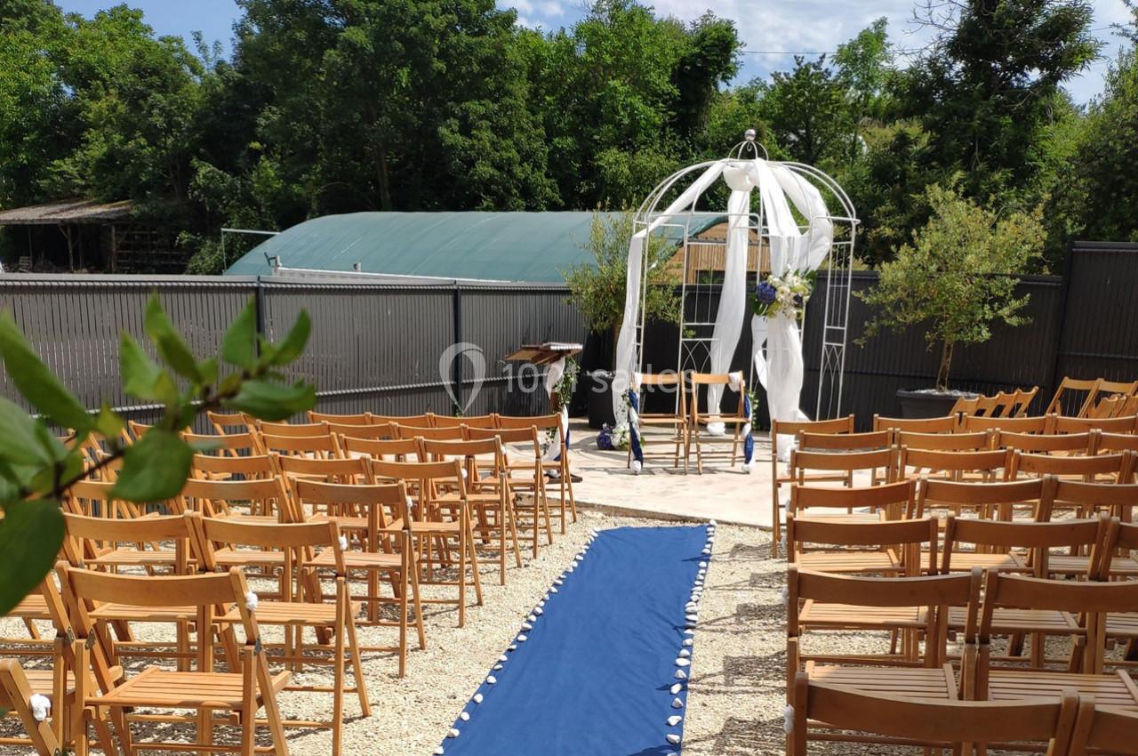 Allée centrale bordée de chaises en bois menant à une arche décorée pour une cérémonie en extérieur.