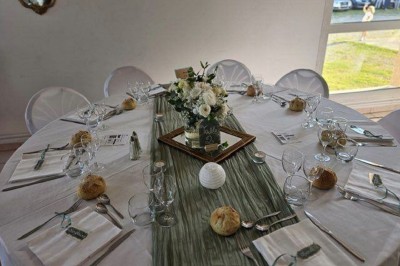 Salle lumineuse avec tables décorées de nappes blanches et chemins de table verts, prête pour un événement.