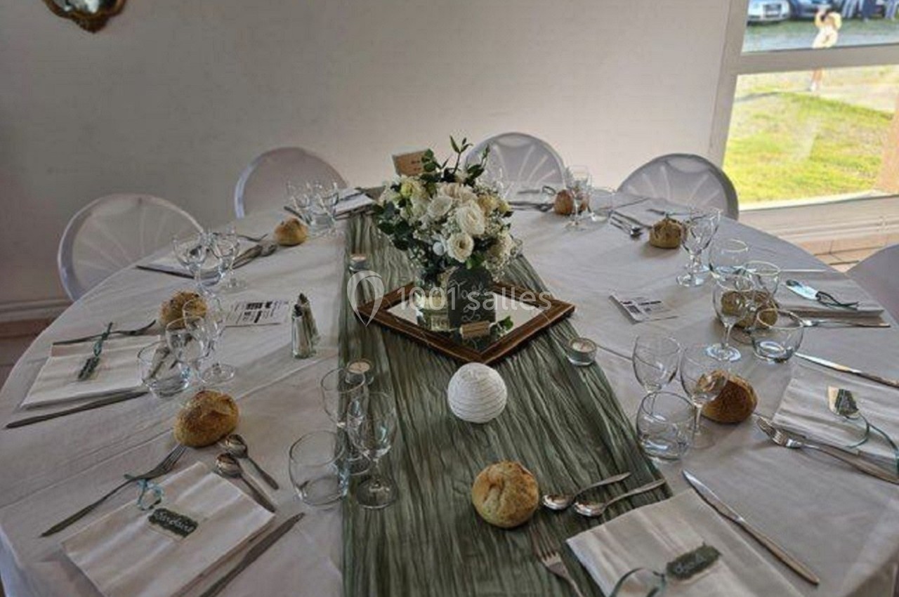 Table ronde dressée pour un repas, décorée avec une nappe blanche, un chemin de table vert et un centre floral.