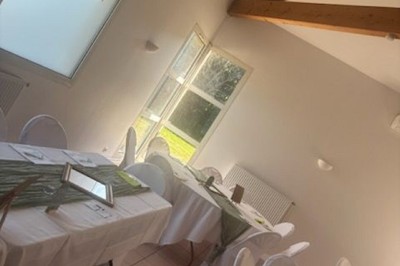 Salle lumineuse avec tables décorées de nappes blanches et chemins de table verts, prête pour un événement.