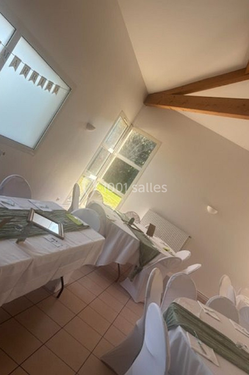 Salle lumineuse avec tables décorées de nappes blanches et chemins de table verts, prête pour un événement.