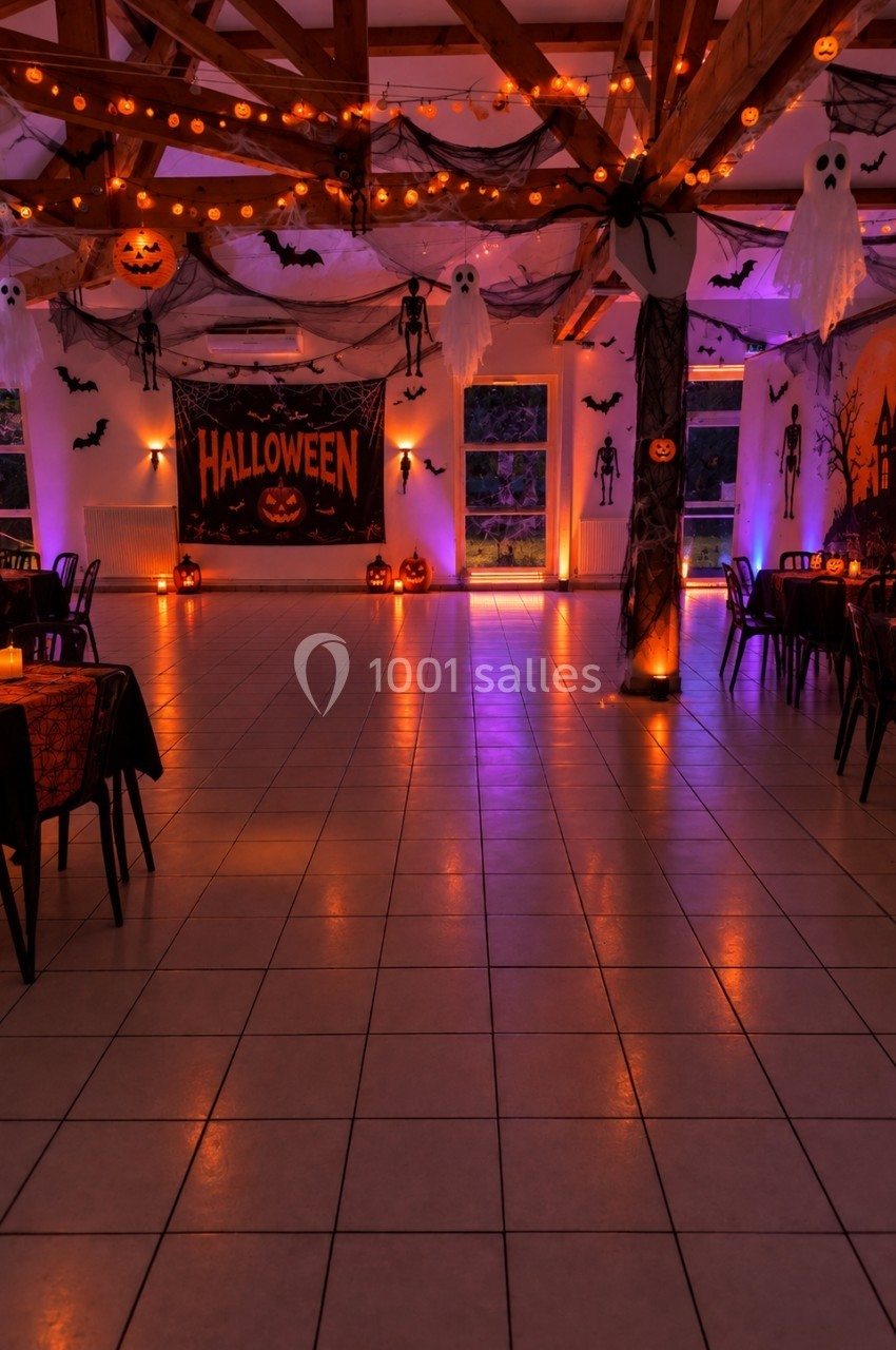 Salle décorée pour Halloween avec guirlandes lumineuses, citrouilles, fantômes suspendus et affiches thématiques.