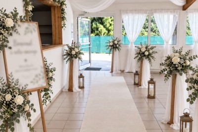 Arche de mariage décorée de fleurs blanches et vertes, avec deux chaises pliantes blanches devant, en extérieur ensoleillé.