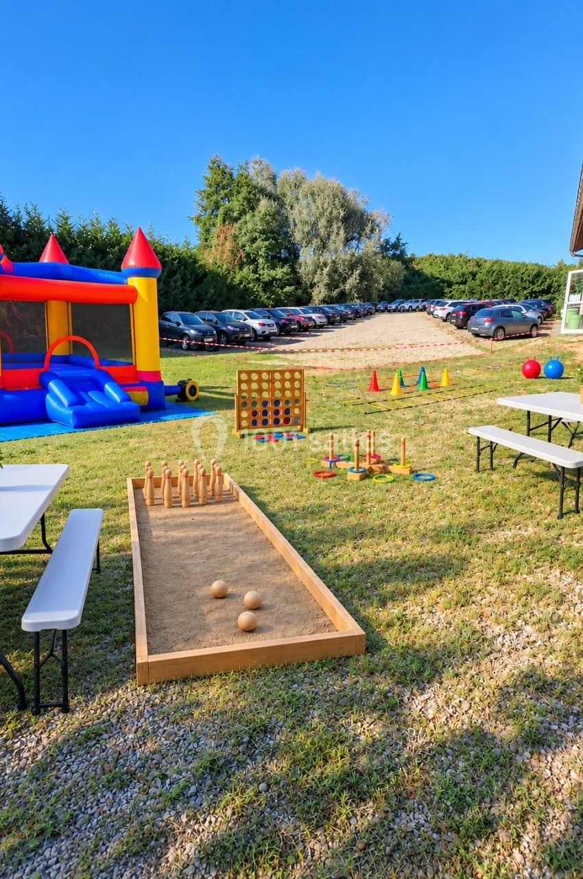 Espace extérieur avec jeux pour enfants : château gonflable, quilles, puissance 4 géant et tables de pique-nique.