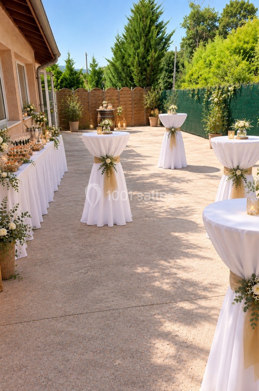Tables hautes décorées de nappes blanches et fleurs, disposées en extérieur pour un événement sous un ciel dégagé.