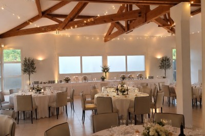 Arche de mariage décorée de fleurs blanches et vertes, avec deux chaises pliantes blanches devant, en extérieur ensoleillé.