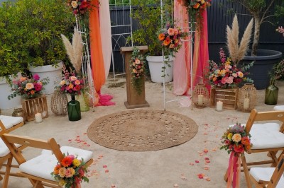 Arche de mariage décorée de fleurs blanches et vertes, avec deux chaises pliantes blanches devant, en extérieur ensoleillé.