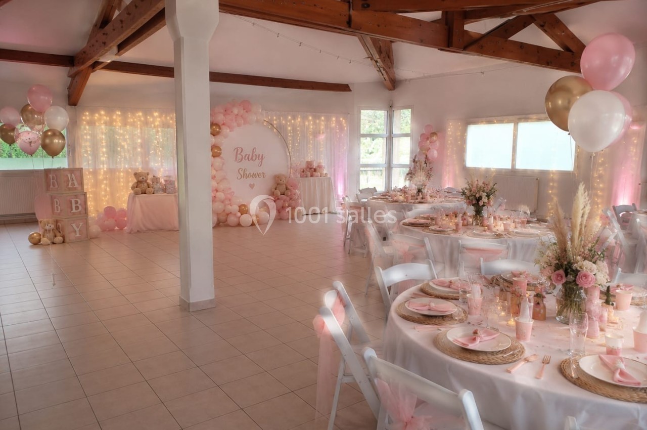 Salle décorée pour une baby shower avec tables dressées, ballons roses et dorés, et guirlandes lumineuses.