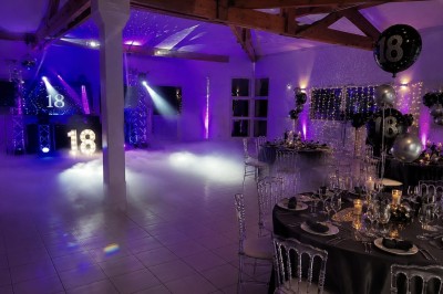 Arche de mariage décorée de fleurs blanches et vertes, avec deux chaises pliantes blanches devant, en extérieur ensoleillé.