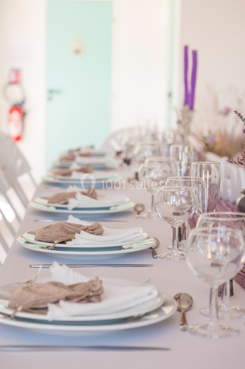 Table dressée avec vaisselle élégante, serviettes pliées et décorations florales dans une salle lumineuse.