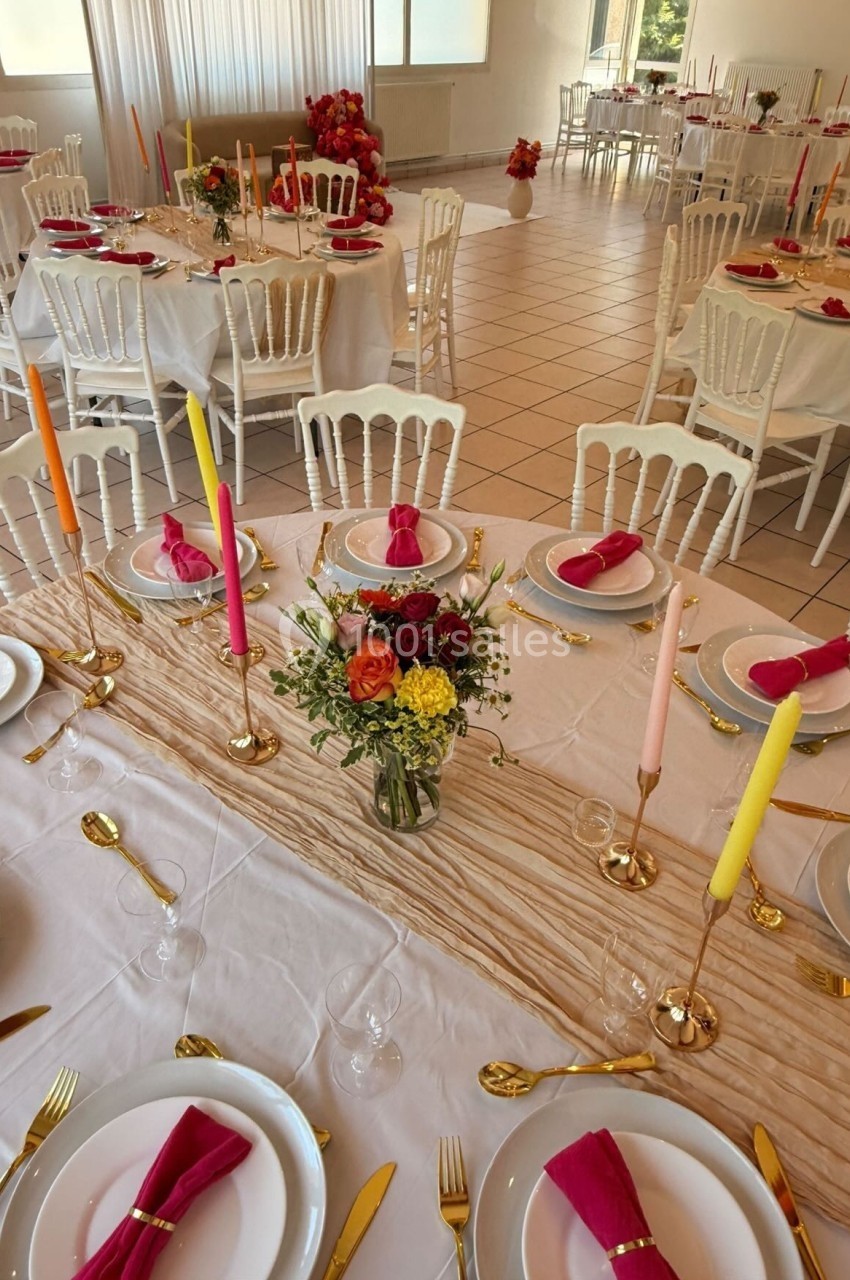 Salle de réception décorée avec des tables dressées, nappes blanches, bougies colorées et compositions florales.