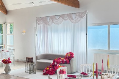 Arche de mariage décorée de fleurs blanches et vertes, avec deux chaises pliantes blanches devant, en extérieur ensoleillé.
