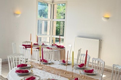 Arche de mariage décorée de fleurs blanches et vertes, avec deux chaises pliantes blanches devant, en extérieur ensoleillé.