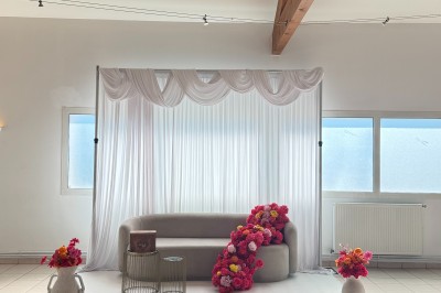 Arche de mariage décorée de fleurs blanches et vertes, avec deux chaises pliantes blanches devant, en extérieur ensoleillé.