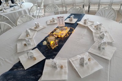 Arche de mariage décorée de fleurs blanches et vertes, avec deux chaises pliantes blanches devant, en extérieur ensoleillé.