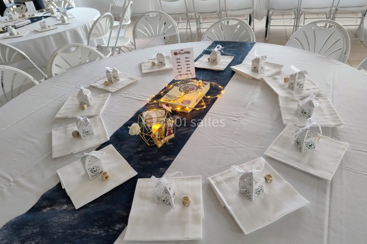 Table décorée avec des nappes blanches, lanternes dorées, bougies et petits cadeaux sur des serviettes pliées.