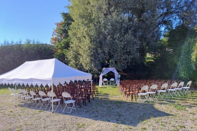 Arche de mariage décorée de fleurs blanches et vertes, avec deux chaises pliantes blanches devant, en extérieur ensoleillé.