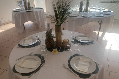 Arche de mariage décorée de fleurs blanches et vertes, avec deux chaises pliantes blanches devant, en extérieur ensoleillé.