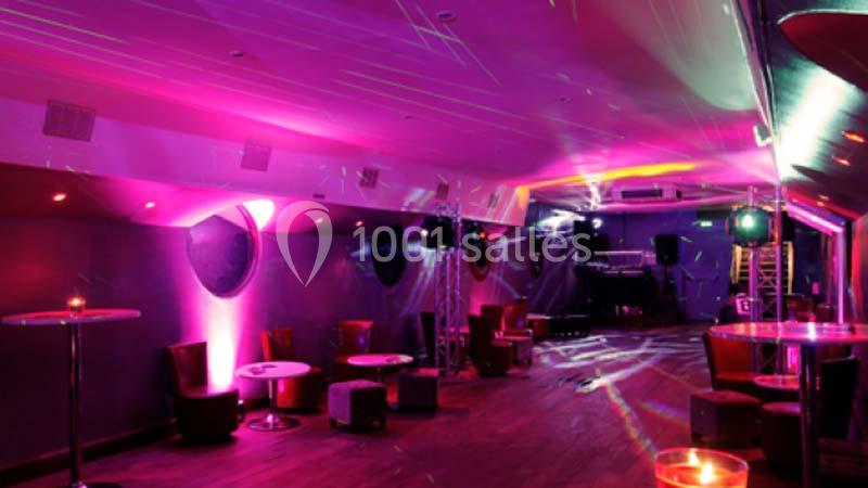 Salle de soirée avec éclairage coloré, tables basses, fauteuils et projecteurs créant une ambiance festive.