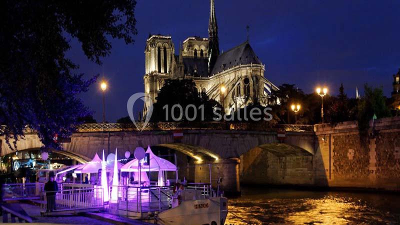 Vue nocturne de Notre-Dame de Paris illuminée, avec un bateau amarré sur la Seine au premier plan.