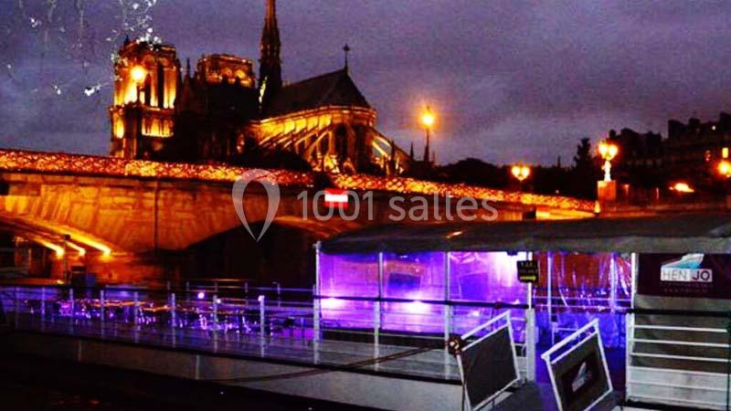 Vue nocturne de Notre-Dame de Paris illuminée, avec un bateau amarré et des lumières colorées sur la Seine.