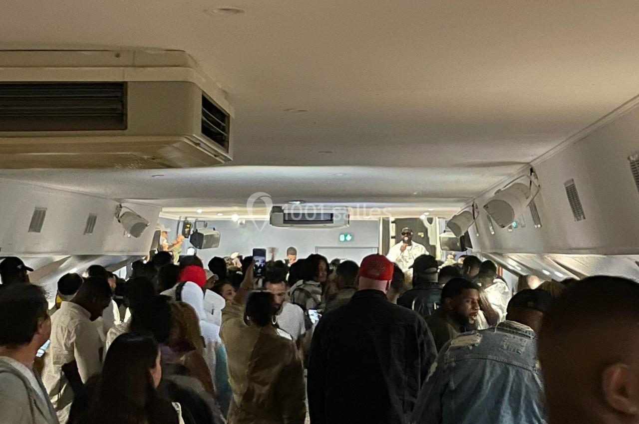 Un groupe de personnes rassemblées dans une salle éclairée, avec un plafond bas et des équipements suspendus.