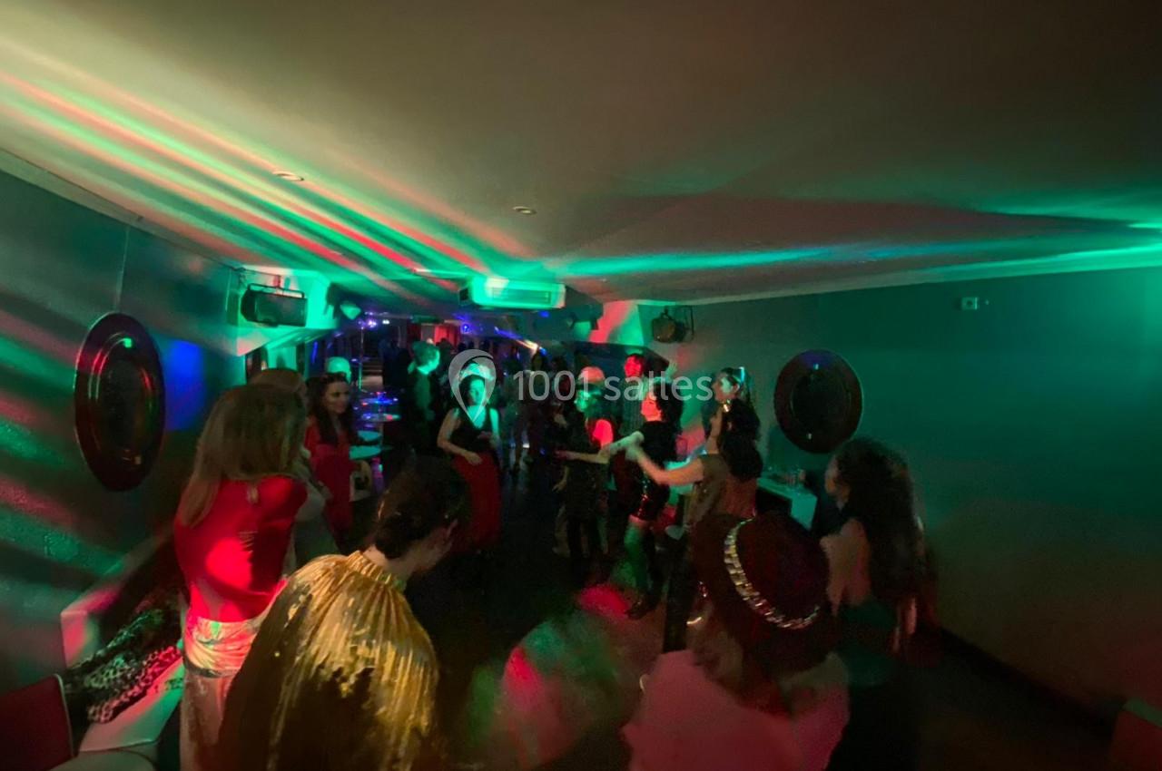 Personnes dansant dans une salle faiblement éclairée avec des lumières colorées créant une ambiance festive.