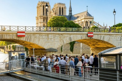 Vue de la cathédrale Notre-Dame de Paris depuis la Seine, entourée d'arbres et reflétée dans l'eau calme.
