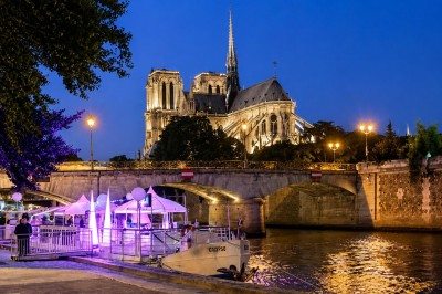 Vue de la cathédrale Notre-Dame de Paris depuis la Seine, entourée d'arbres et reflétée dans l'eau calme.