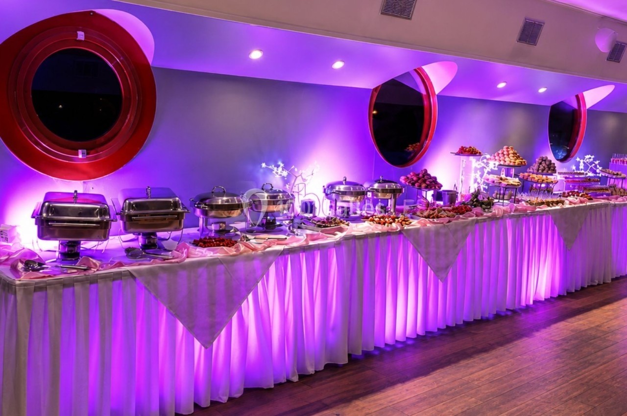 Buffet varié avec plats chauds et froids disposés sur une longue table éclairée par une lumière violette.