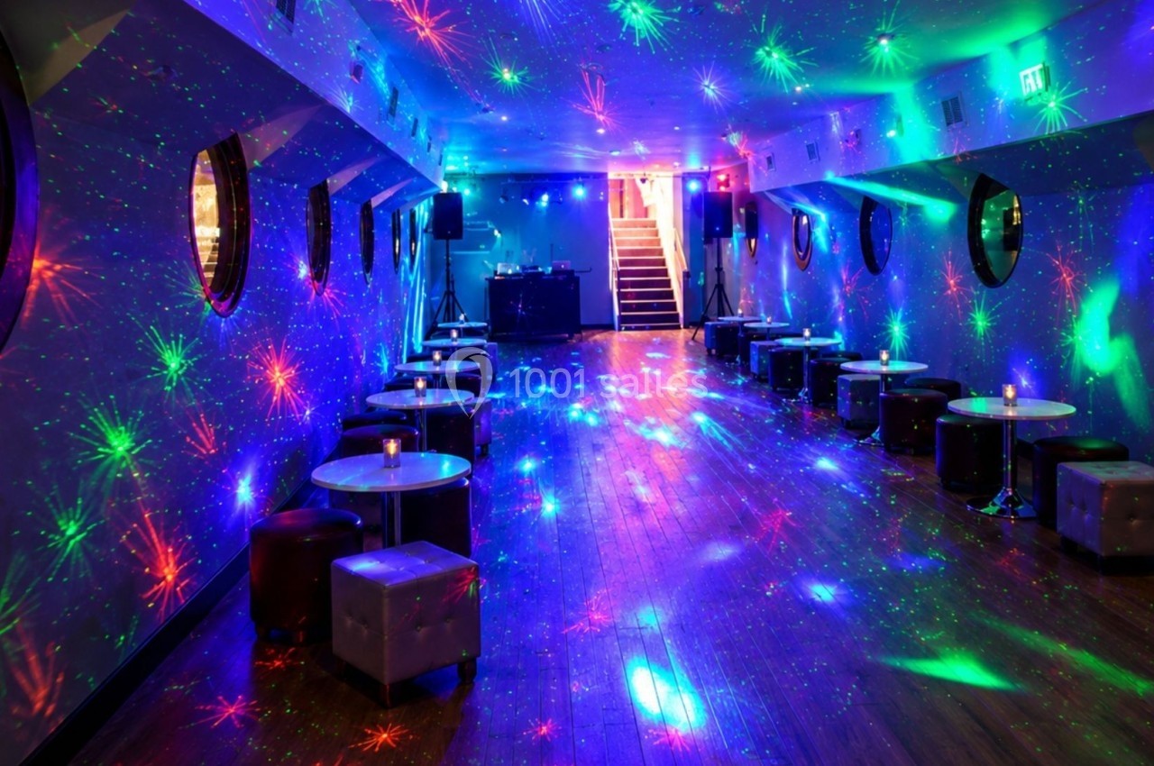 Salle avec tables basses et jeux de lumières colorées projetés sur les murs et le sol, ambiance festive.
