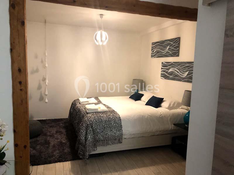 Chambre lumineuse avec un lit double, décorée de tableaux abstraits, lampes de chevet et linge de lit plié.