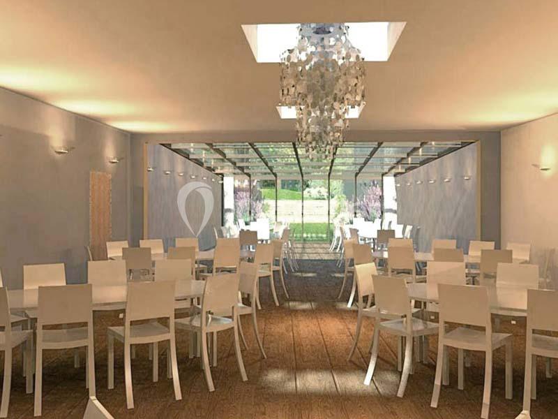 Salle lumineuse avec des chaises blanches alignées autour de tables, un lustre central et une vue sur un jardin.