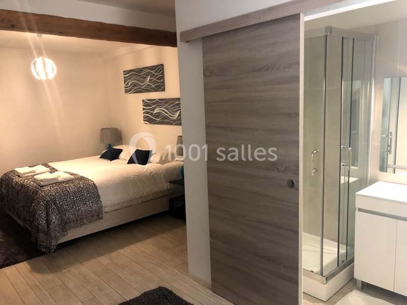 Chambre avec lit double, salle de bain attenante avec douche vitrée et lavabo, décor moderne et épuré.