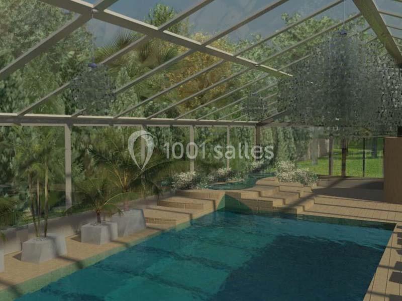 Piscine intérieure avec verrière, entourée de plantes et de végétation extérieure visible à travers les vitres.