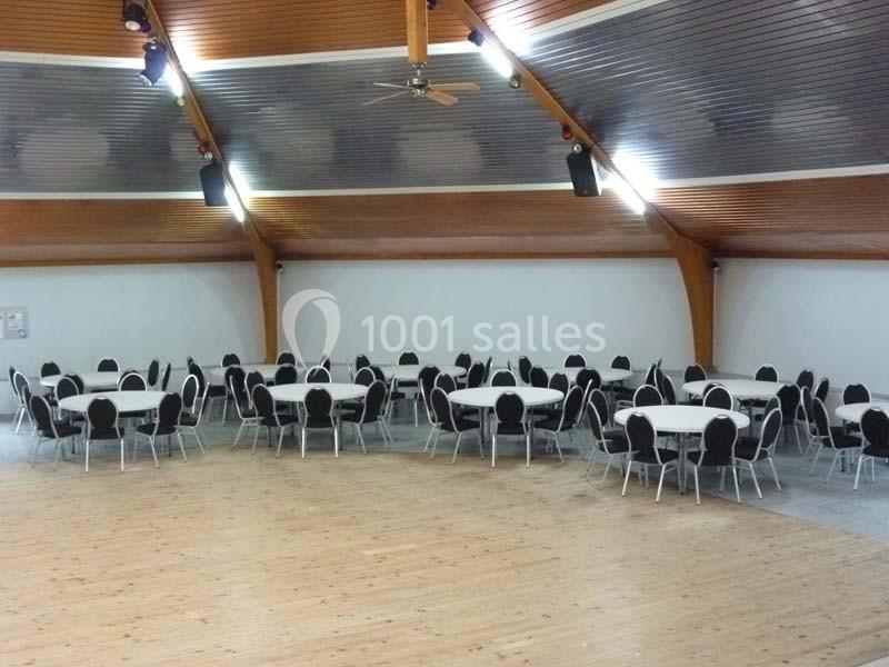 Salle circulaire avec plafond en bois, tables rondes et chaises noires disposées pour un événement.