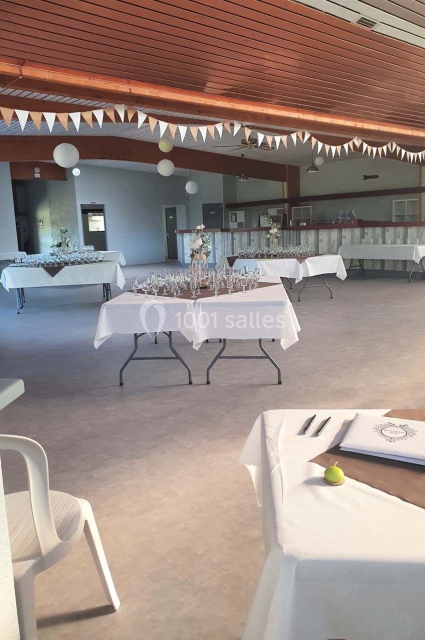 Salle de réception décorée avec des tables nappées de blanc, ornées de verres et de décorations festives.