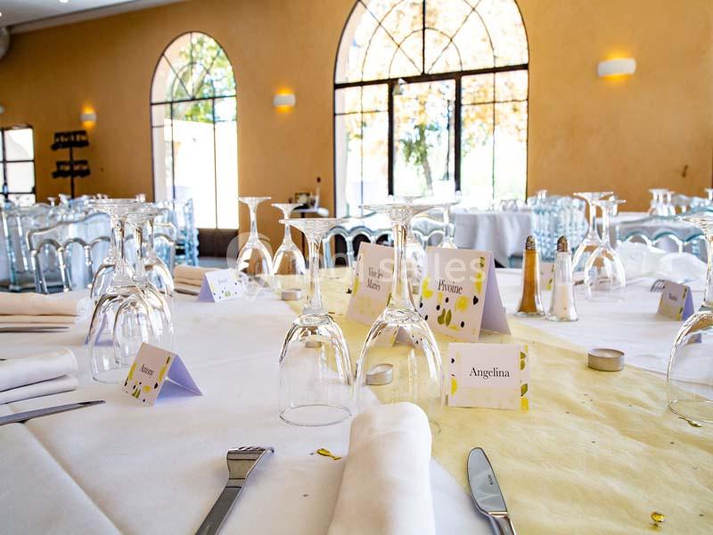 Table dressée pour un événement avec nappes blanches, verres retournés, couverts et marque-places personnalisés.
