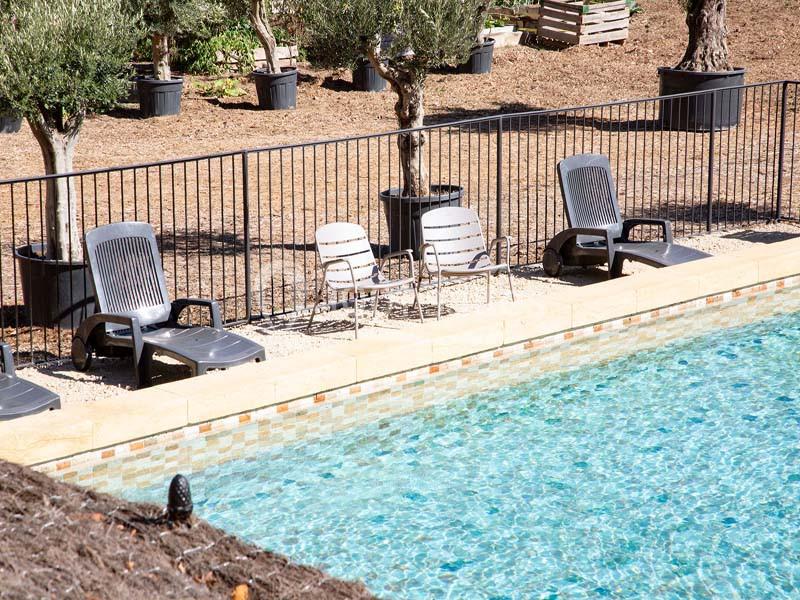 Chaises longues et fauteuils disposés près d'une piscine entourée d'une clôture et d'arbres en pots.